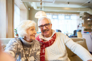 Portrait of happy senior couple holding camera and taking selfie photo on Christmas sitting in cafe